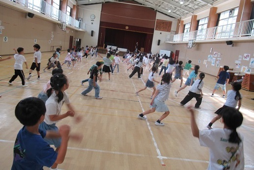 児童が、舞台上に立つダンスの先生を真似て踊っています。