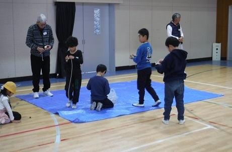 児童が地域の方にコマ回しのやり方を教わっています。